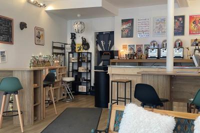 Intérieur d'un café cosy avec comptoir, tabourets, tables en bois et décorations murales variées.