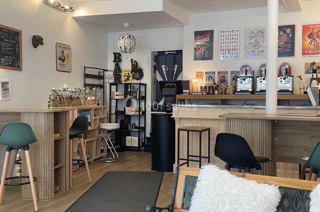 Intérieur d'un café cosy avec comptoir, tabourets, tables en bois et décorations murales variées.