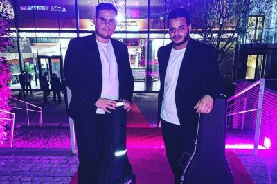 Trois hommes debout dans un jardin jouent de la guitare acoustique, vêtus de chemises blanches.