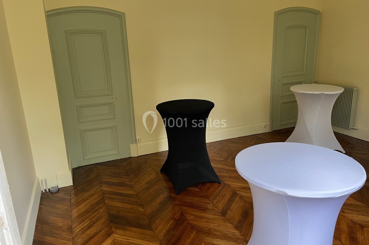 Trois tables hautes recouvertes de housses noires et blanches dans une pièce au parquet en chevrons et murs clairs.