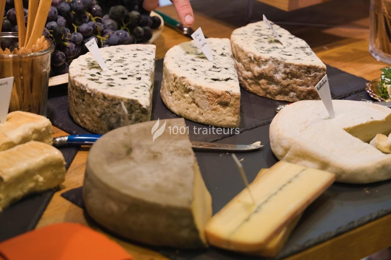 Assortiment de fromages variés présentés sur une table, avec étiquettes et raisins en arrière-plan.