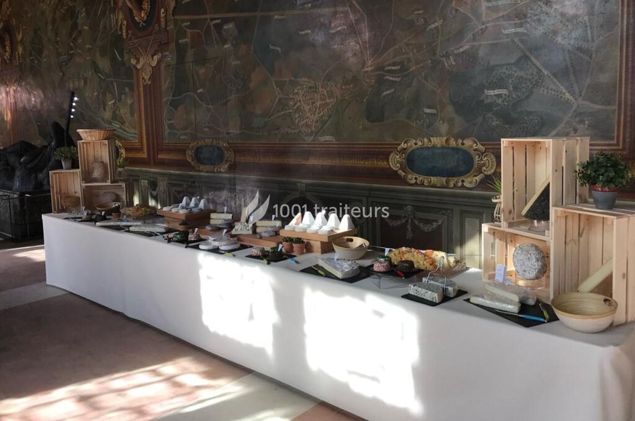 Table de buffet élégamment dressée avec divers fromages, présentée devant une fresque murale décorative.