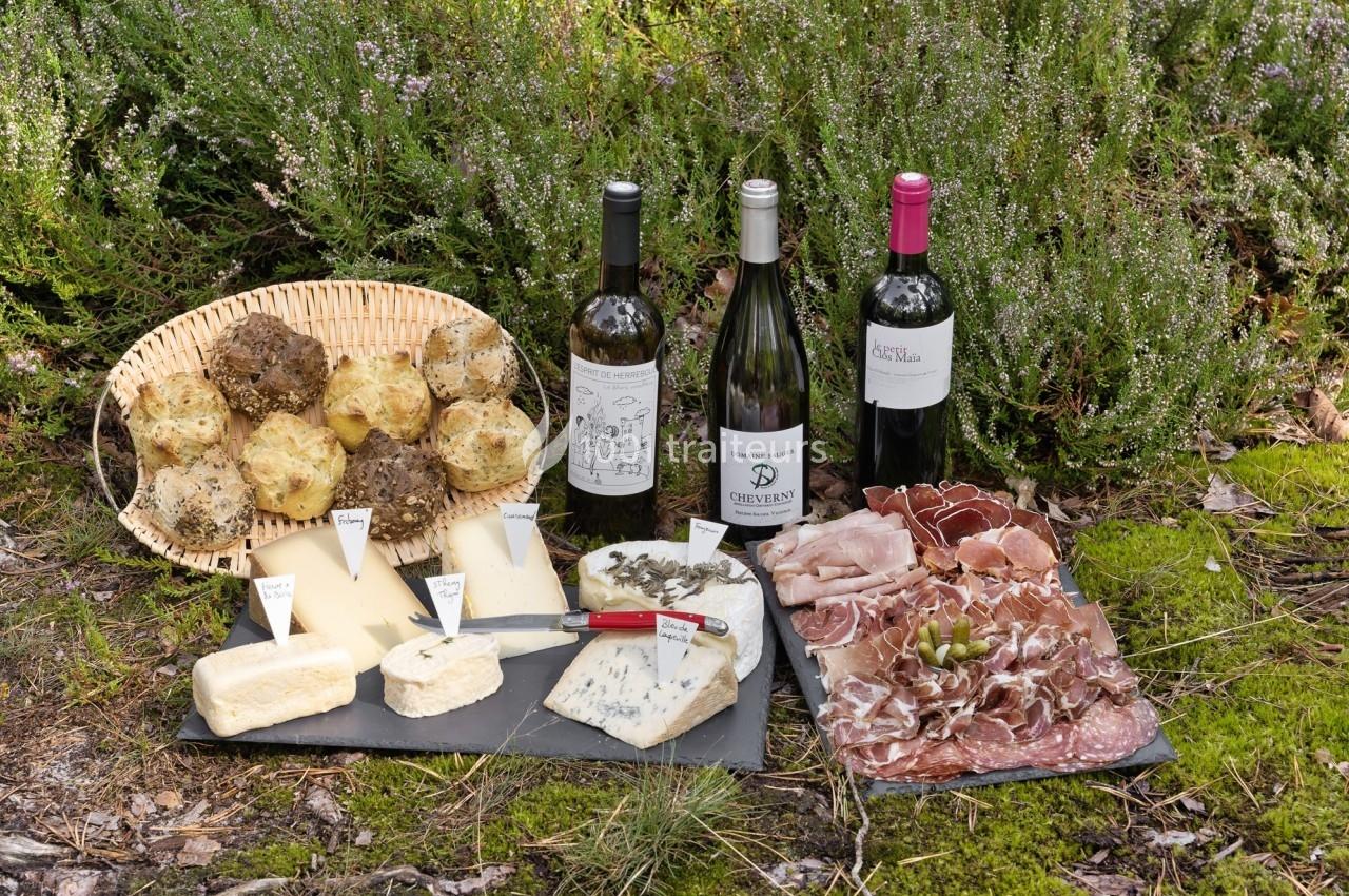 Plateau de fromages variés, charcuteries, truffes, et trois bouteilles de vin disposés sur un sol naturel.