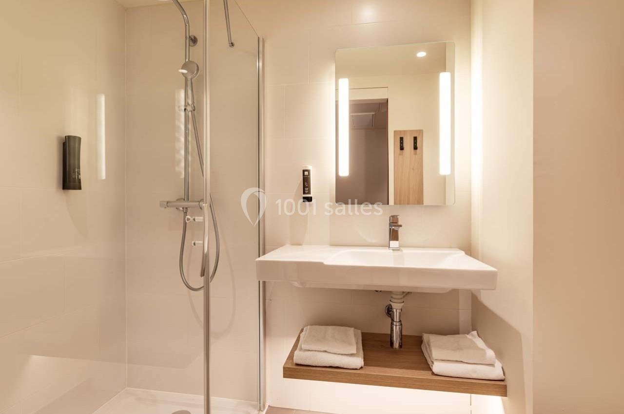 Salle de bain moderne avec douche à l'italienne, lavabo suspendu, miroir éclairé et étagère avec serviettes.