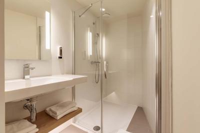 Salle de bain moderne avec douche à l'italienne, lavabo avec miroir éclairé et serviettes pliées sur une étagère.