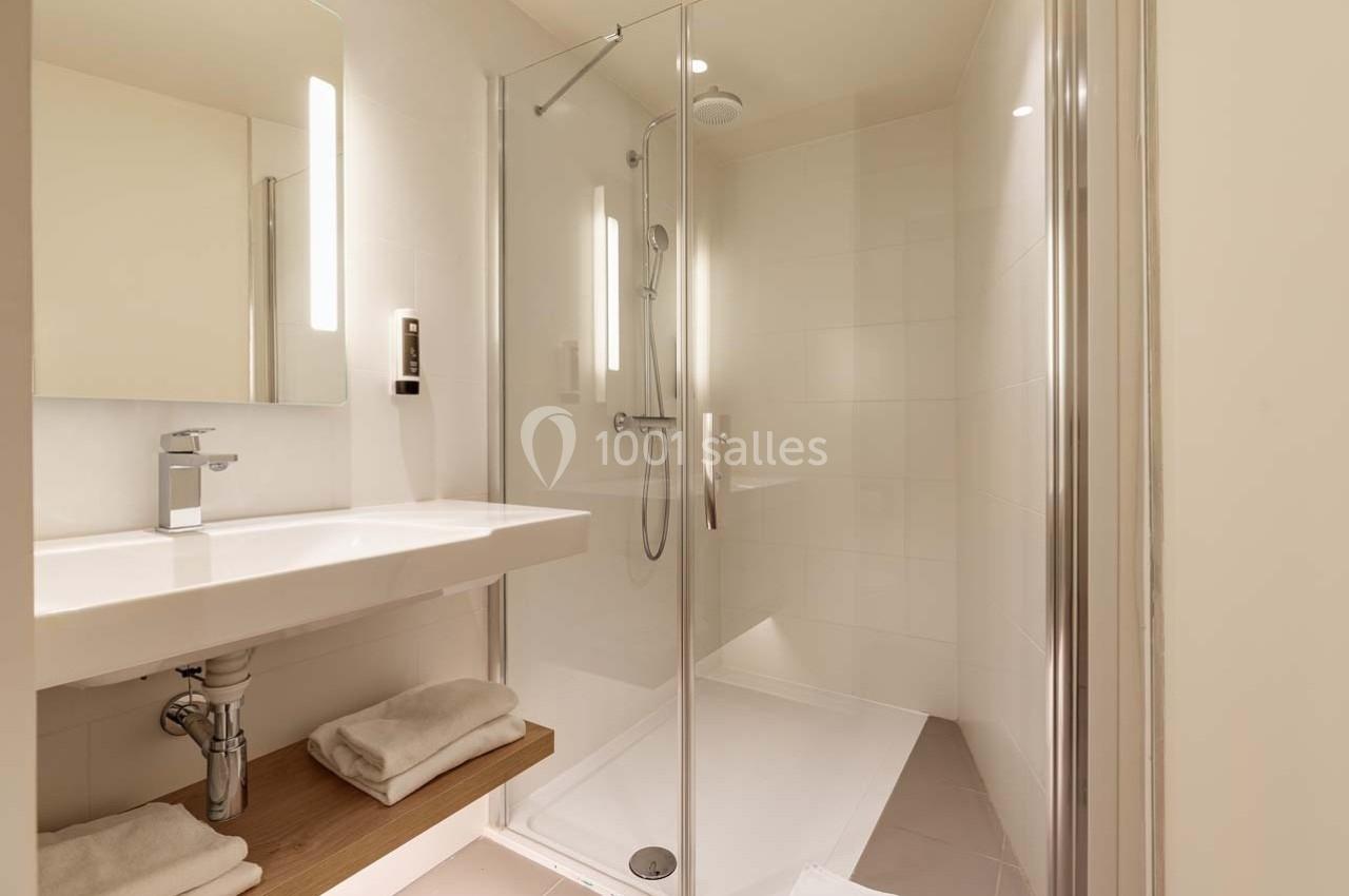 Salle de bain moderne avec douche à l'italienne, lavabo avec miroir éclairé et serviettes pliées sur une étagère.