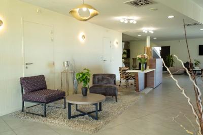 Terrasse en bois avec table, chaises et parasol, entourée de plantes, devant une façade en bois sous un ciel bleu.