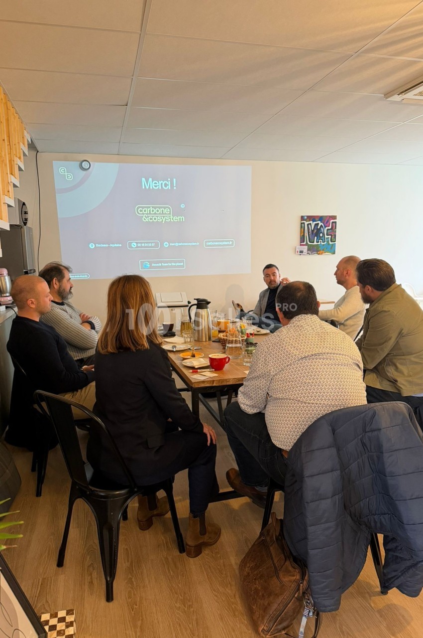 Un groupe de personnes assises autour d'une table en réunion dans une salle équipée d'un projecteur.