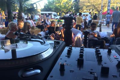 Terrasse couverte avec piste de danse, tables hautes, décoration lumineuse et équipement de DJ au premier plan.