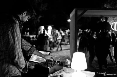 Un DJ mixe de la musique sur une table de mixage lors d'un événement en extérieur, éclairé par une lampe.