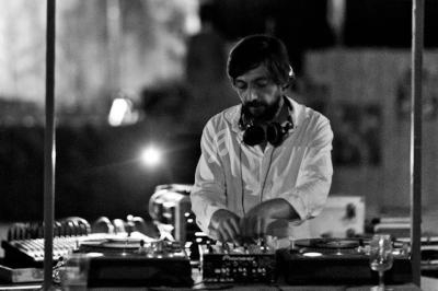 Un DJ en chemise blanche mixe de la musique sur des platines dans un environnement sombre.