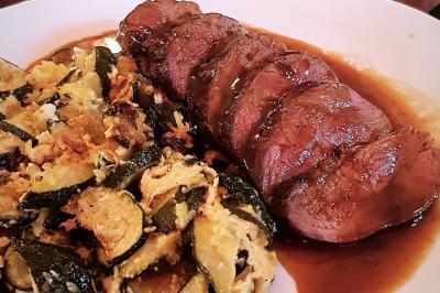 Deux choux farcis servis dans une assiette blanche avec une sauce brune, sur une table en bois.