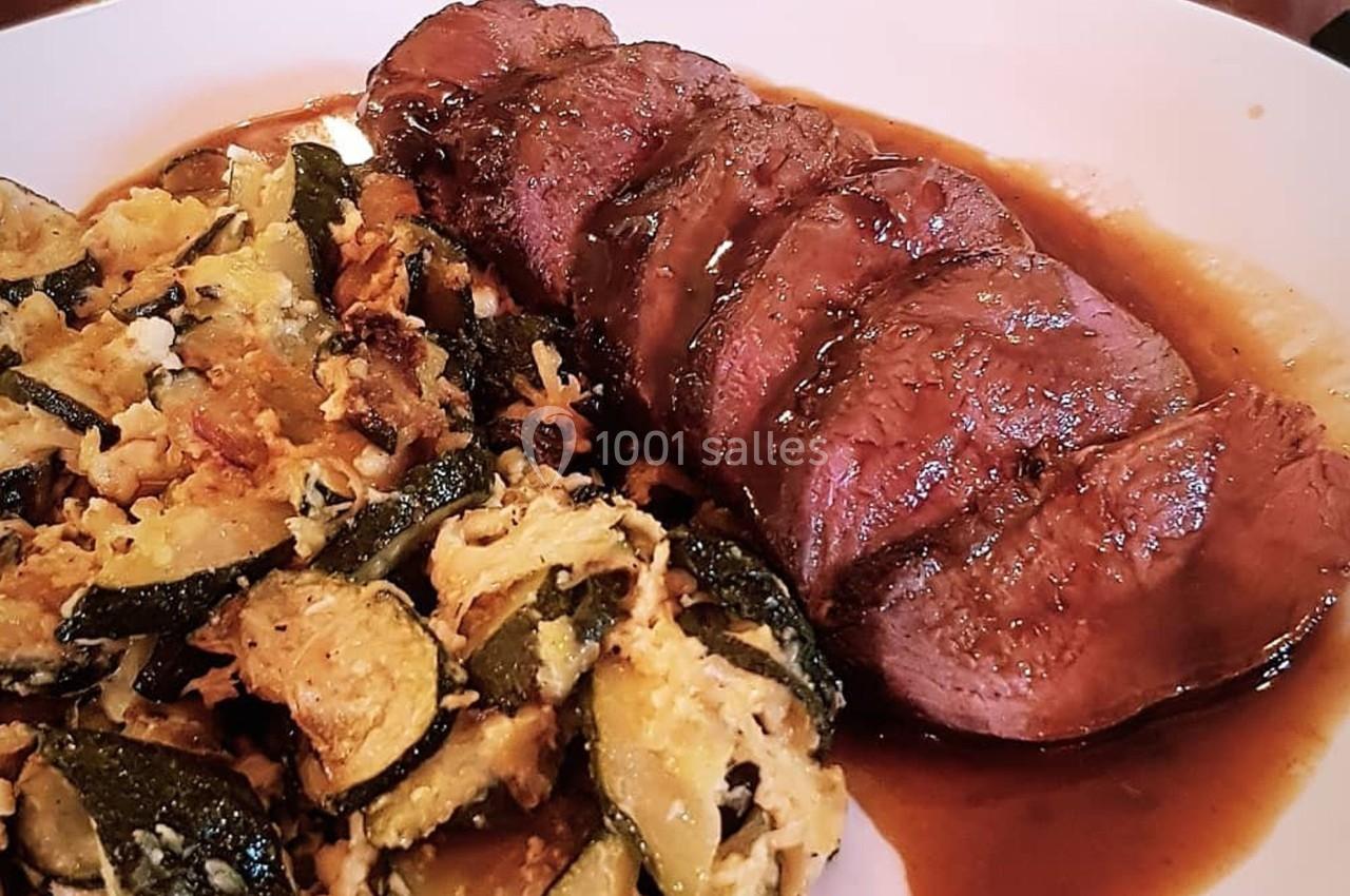 Tranches de viande nappées de sauce brune, accompagnées de courgettes sautées dans une assiette blanche.