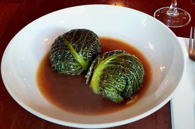 Deux choux farcis servis dans une assiette blanche avec une sauce brune, sur une table en bois.
