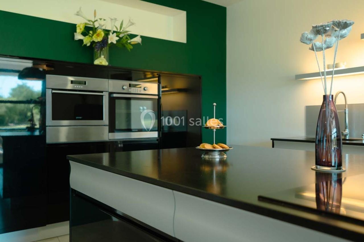 Cuisine moderne avec îlot central, four encastré, plan de travail noir et décoration florale.