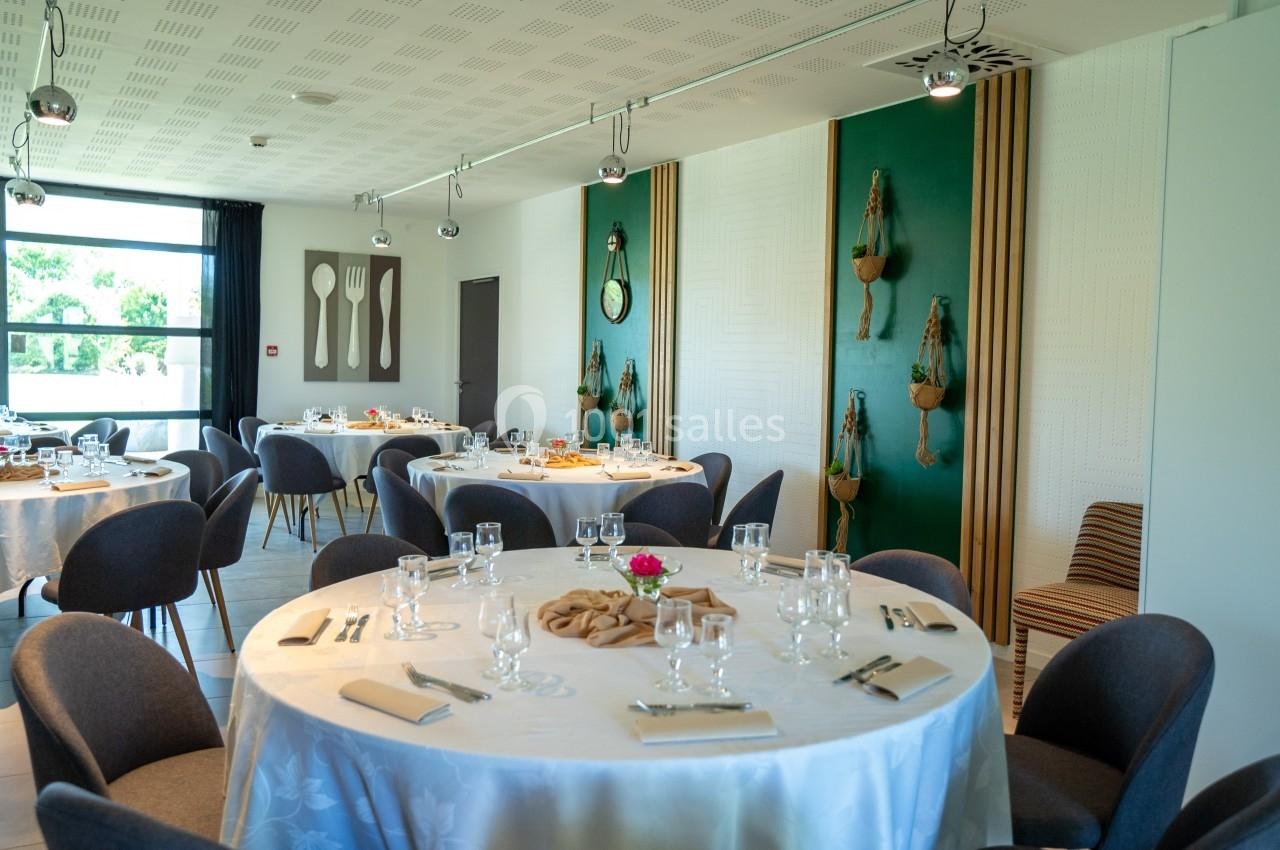 Salle de réception lumineuse avec tables rondes dressées, chaises modernes et décoration murale végétale.