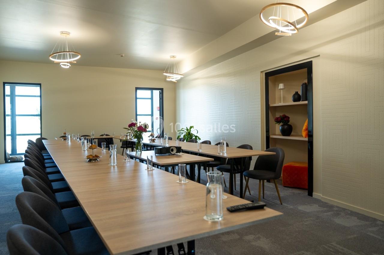 Salle de réunion lumineuse avec une longue table en bois, chaises noires, bouteilles d'eau et décoration sobre.