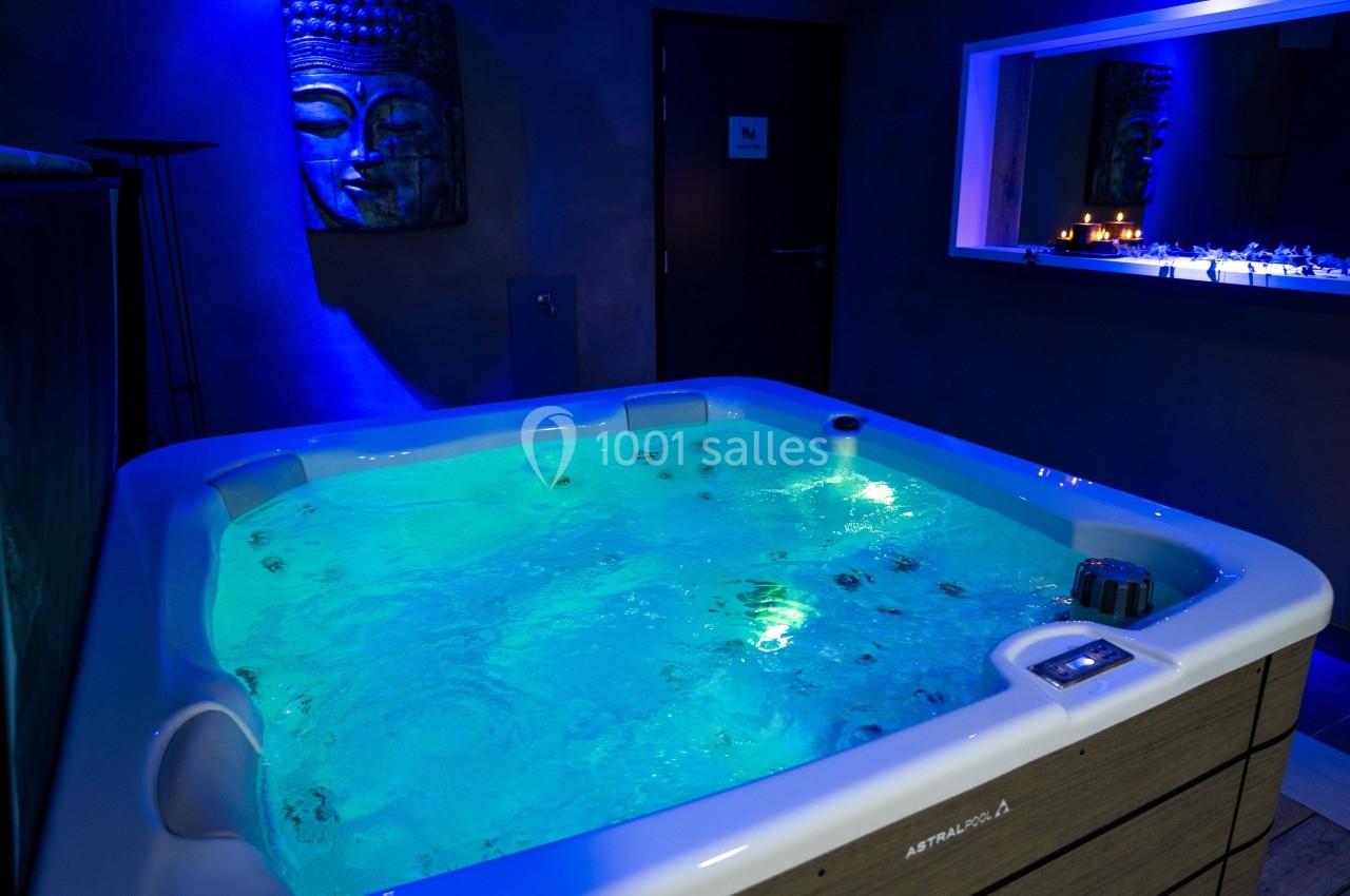 Bain à remous éclairé dans une pièce sombre avec une décoration murale et une ambiance relaxante.