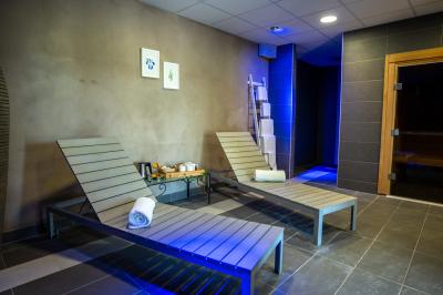 Deux chaises longues en métal avec serviettes roulées dans un espace spa, près d'un sauna en bois.