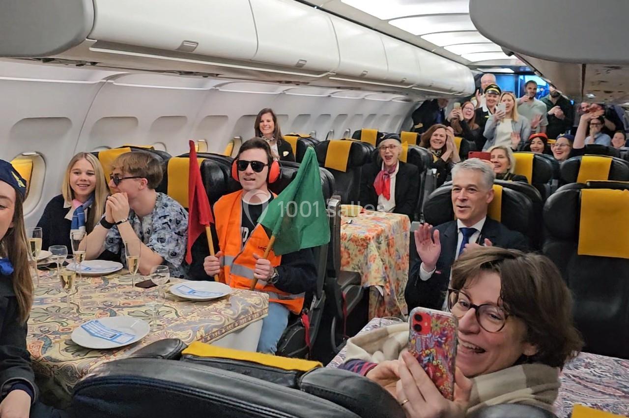 Des passagers souriants dans un avion, certains tenant des drapeaux, d'autres prenant des photos ou applaudissant.
