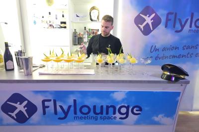 Salle d'exposition avec des stands, des écrans interactifs et des tables hautes, décorée de nuages suspendus.