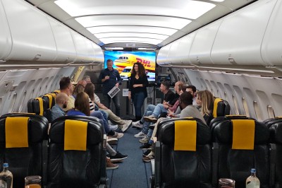 Salle d'exposition avec des stands, des écrans interactifs et des tables hautes, décorée de nuages suspendus.