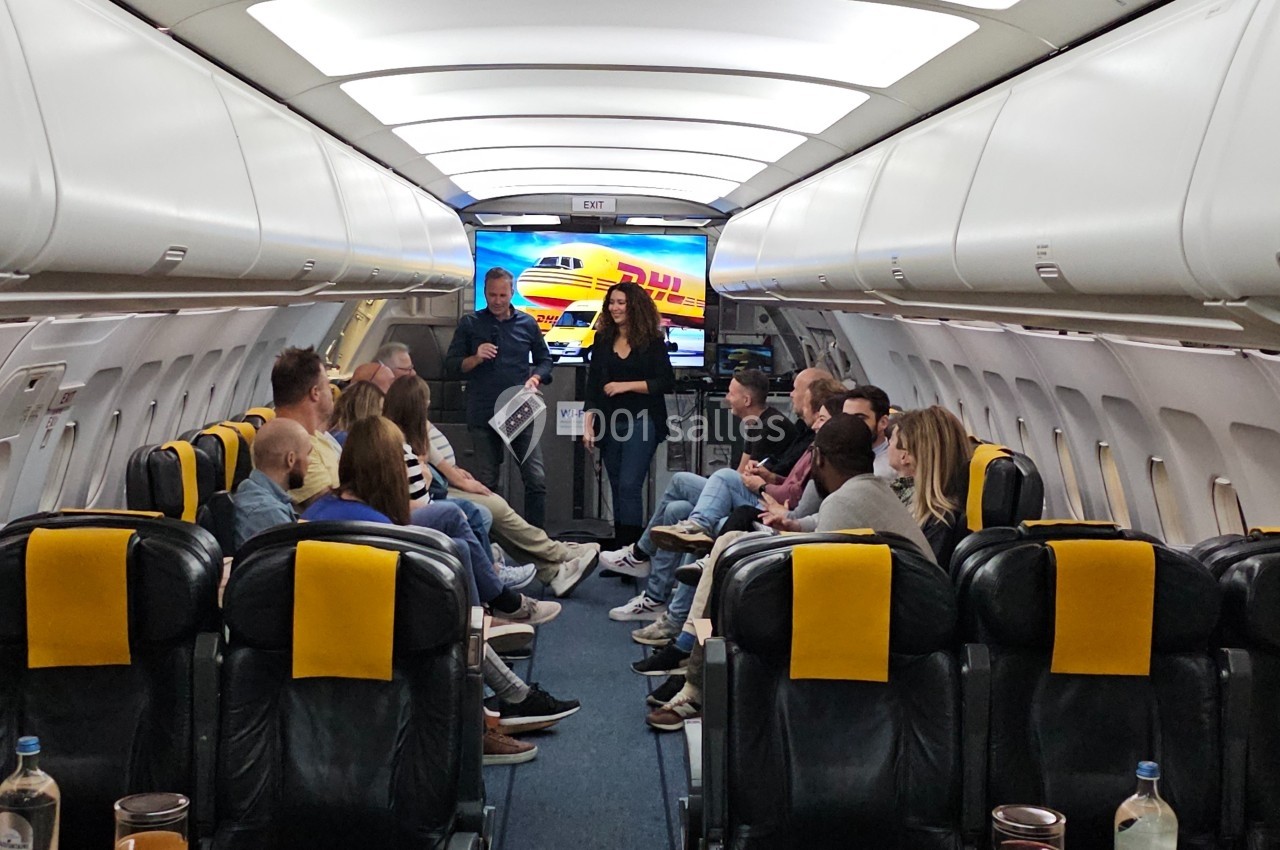 Intérieur d'un avion aménagé avec des sièges en cuir noir et des personnes participant à une discussion en groupe.