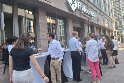 Salle d'exposition avec des stands, des écrans interactifs et des tables hautes, décorée de nuages suspendus.