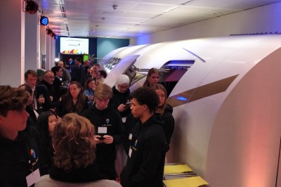 Salle d'exposition avec des stands, des écrans interactifs et des tables hautes, décorée de nuages suspendus.