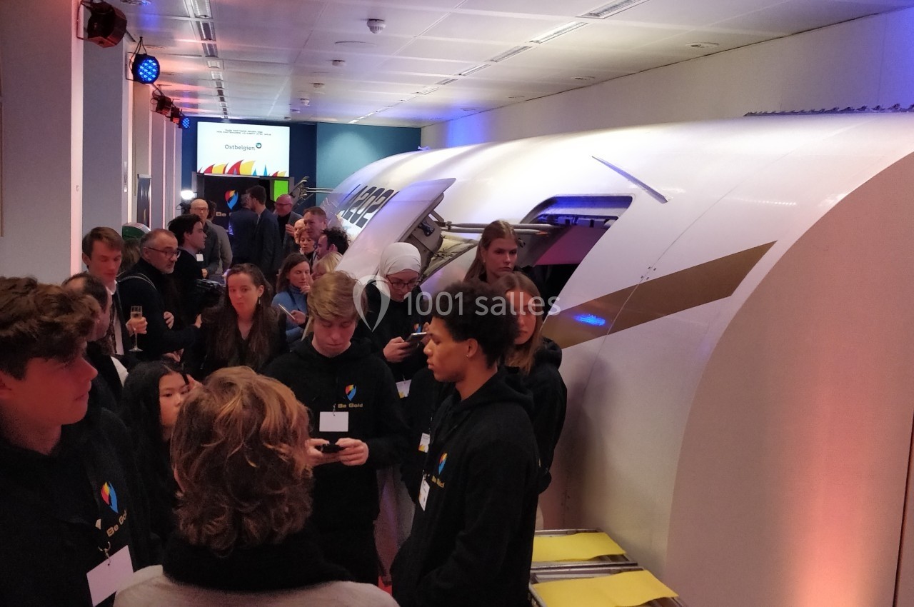 Des visiteurs échangent avec des jeunes devant une maquette de train futuriste dans un espace d'exposition éclairé.