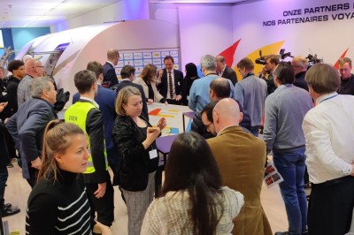 Salle d'exposition avec des stands, des écrans interactifs et des tables hautes, décorée de nuages suspendus.