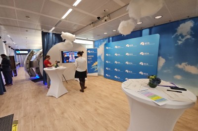 Salle d'exposition avec des stands, des écrans interactifs et des tables hautes, décorée de nuages suspendus.