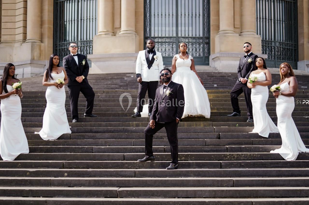 Un groupe de mariés et témoins posant sur des marches devant un bâtiment à colonnes.