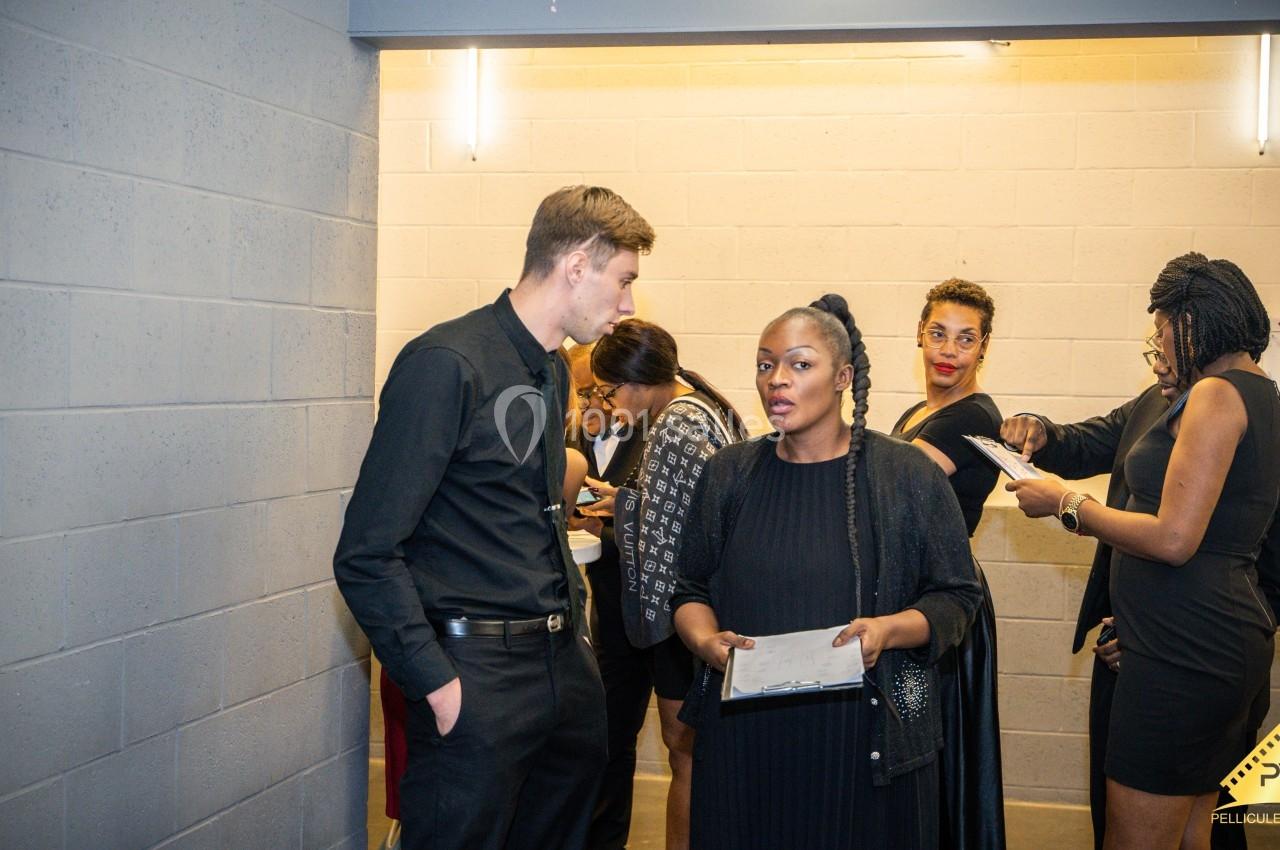 Un groupe de personnes en tenue formelle discute dans un couloir éclairé, certaines tenant des documents.