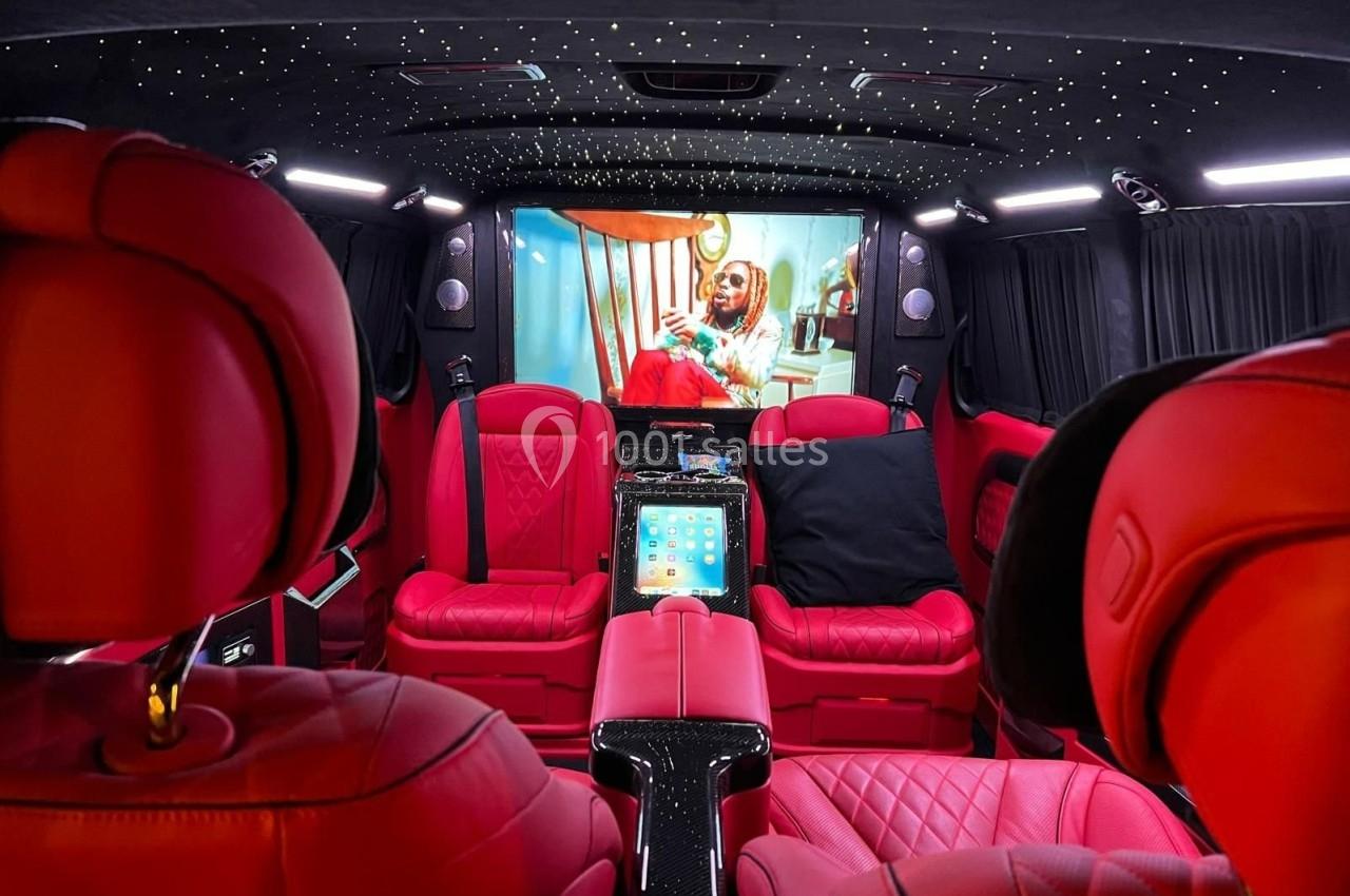 Intérieur d'un véhicule luxueux avec sièges en cuir rouge, éclairage étoilé et écran affichant une vidéo.