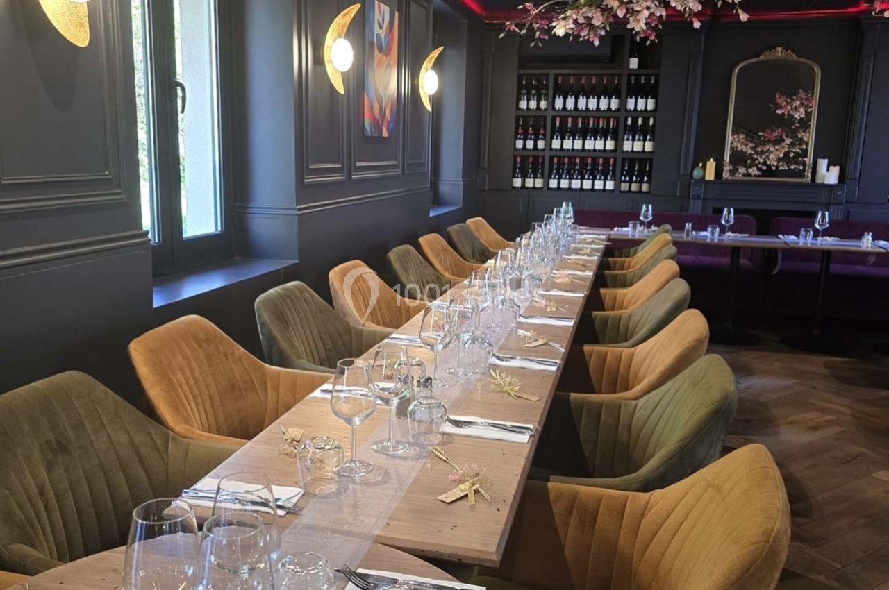 Salle de restaurant élégante avec une longue table dressée, entourée de chaises colorées et éclairée par une lumière douce.
