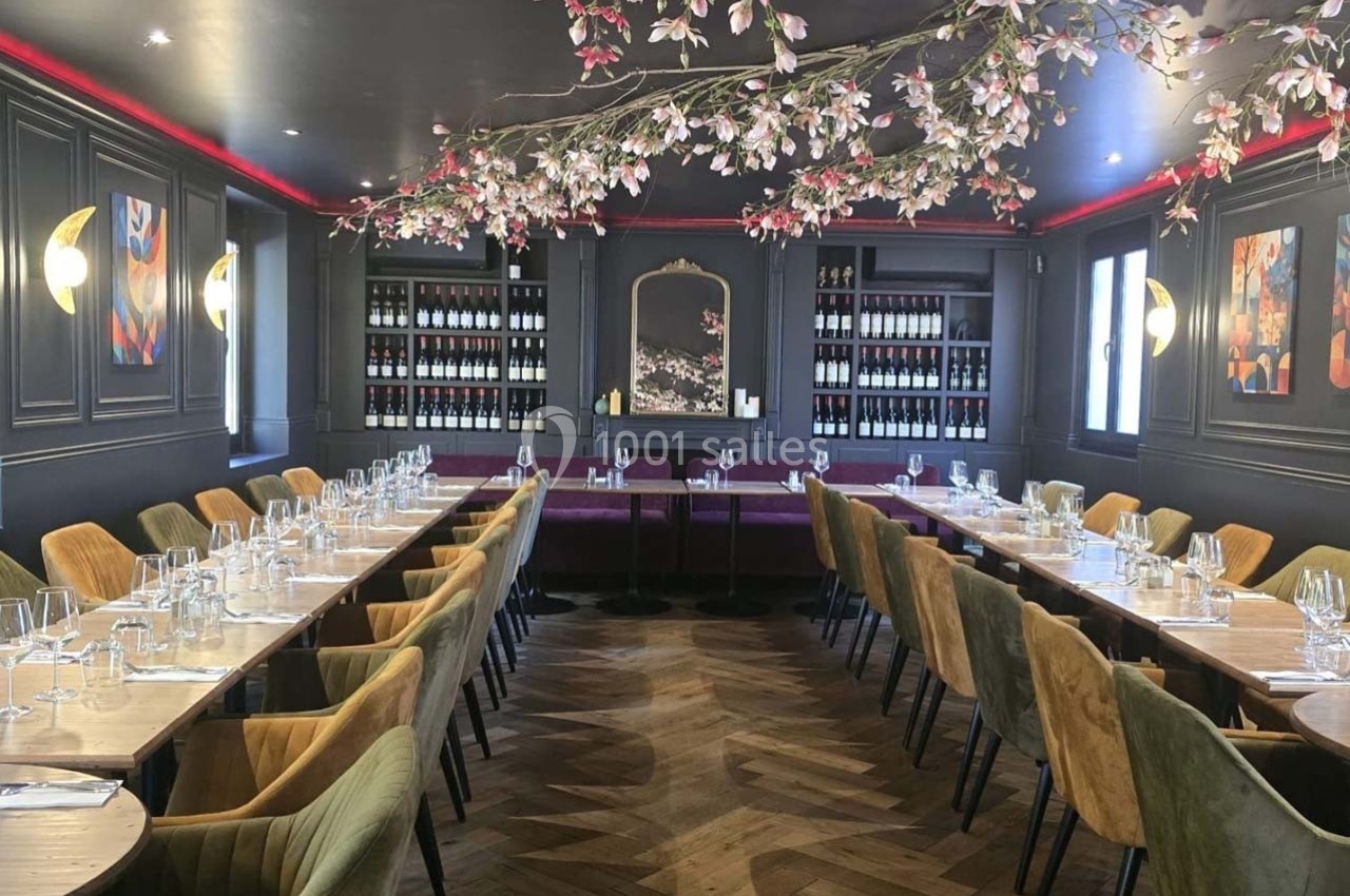 Salle de restaurant élégante avec tables dressées, chaises en velours, éclairage doux et décoration florale suspendue.