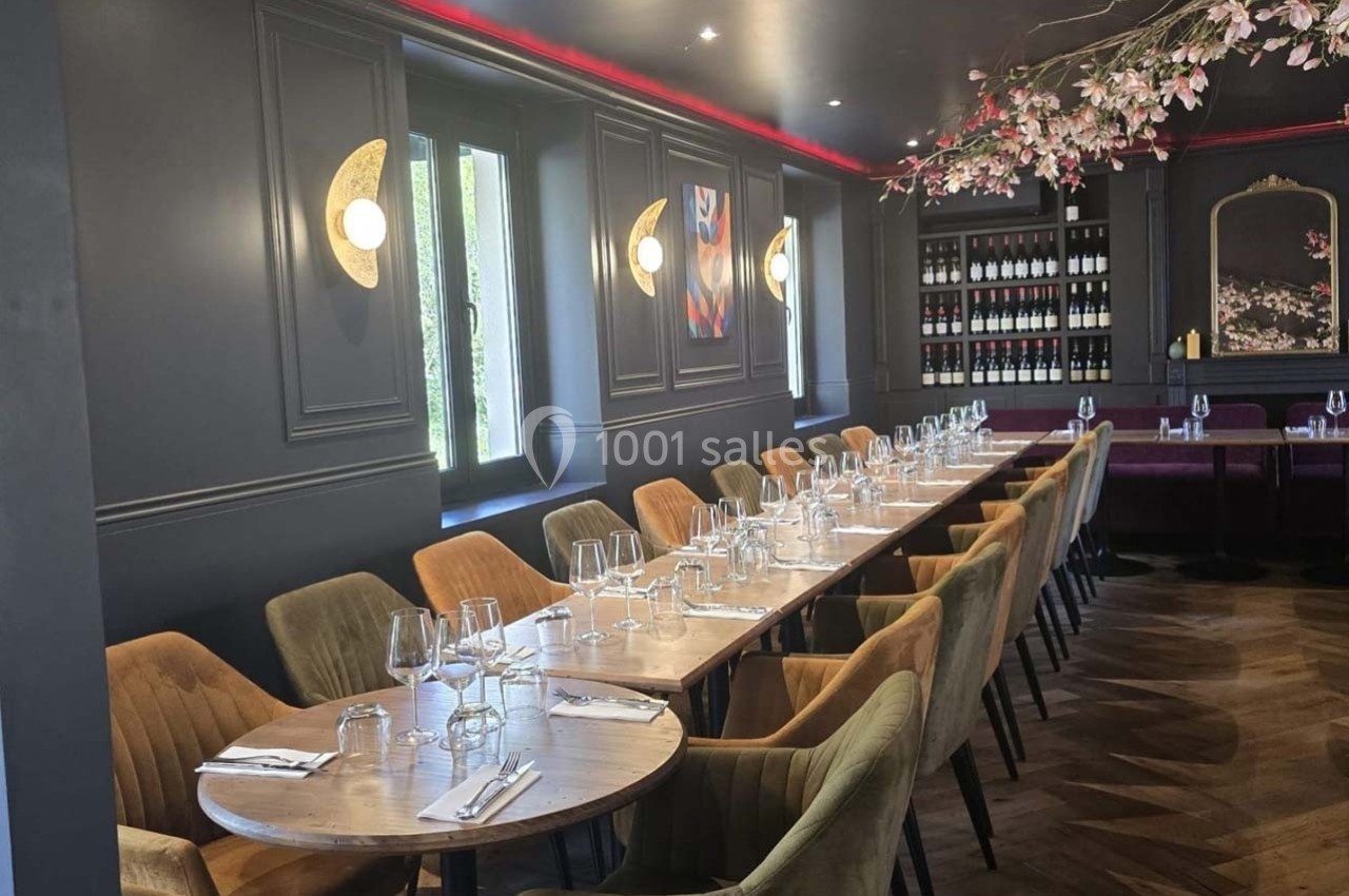 Salle de restaurant élégante avec tables alignées, chaises rembourrées, éclairage mural et décoration florale suspendue.