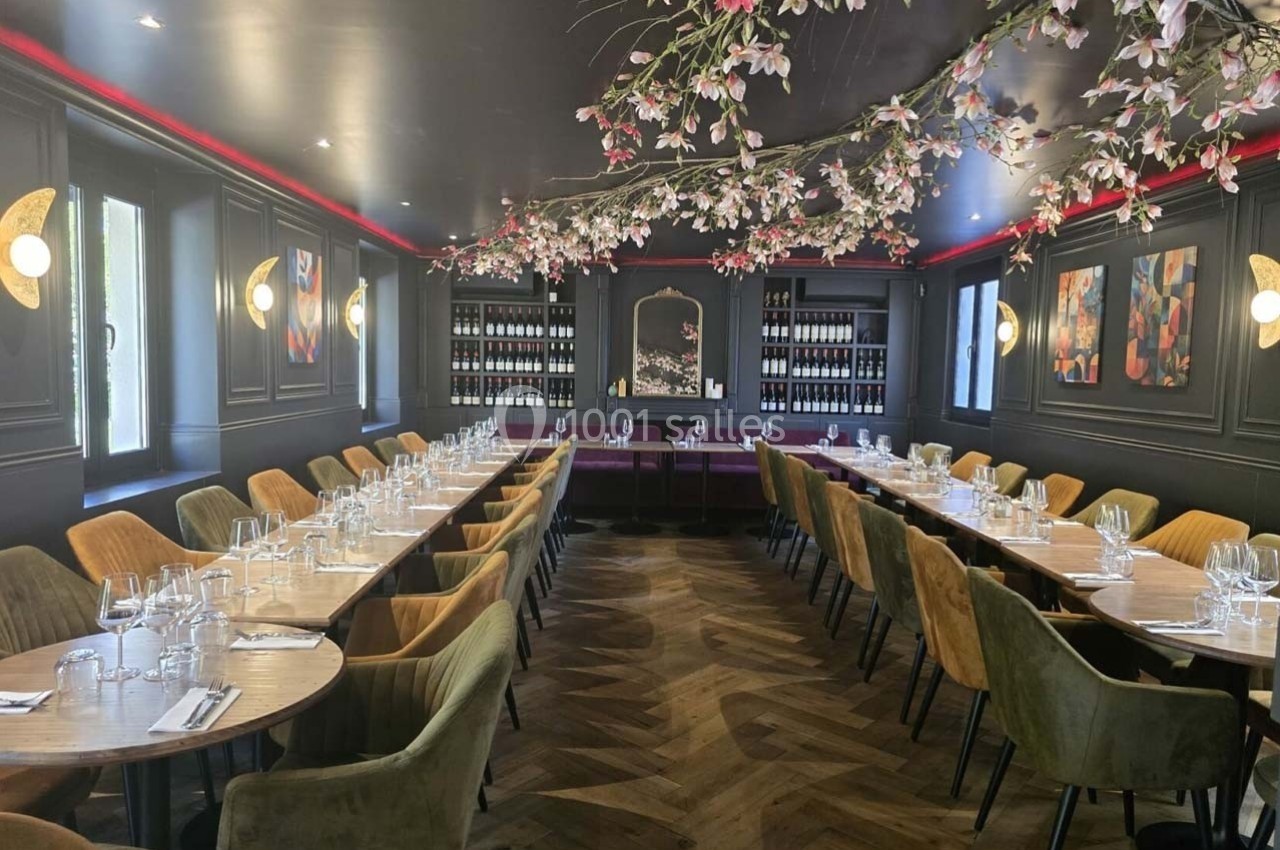 Salle de restaurant élégante avec tables alignées, chaises colorées, éclairage tamisé et décoration florale suspendue.