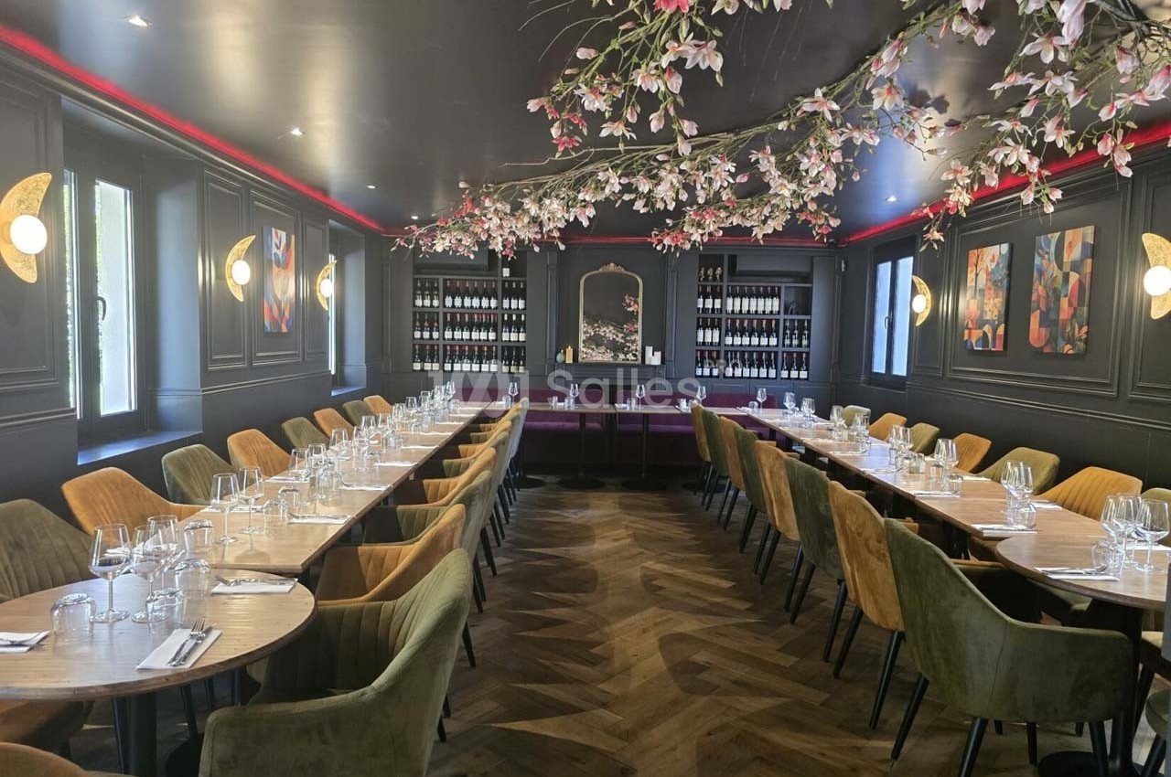 Salle de restaurant élégante avec tables alignées, chaises colorées, éclairage tamisé et décoration florale suspendue.