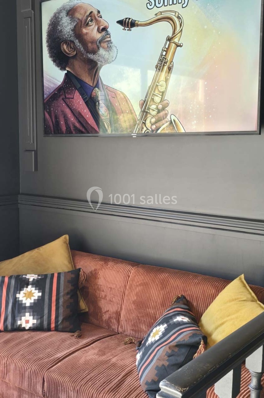 Canapé en velours côtelé marron avec coussins colorés, sous un tableau représentant un musicien jouant du saxophone.