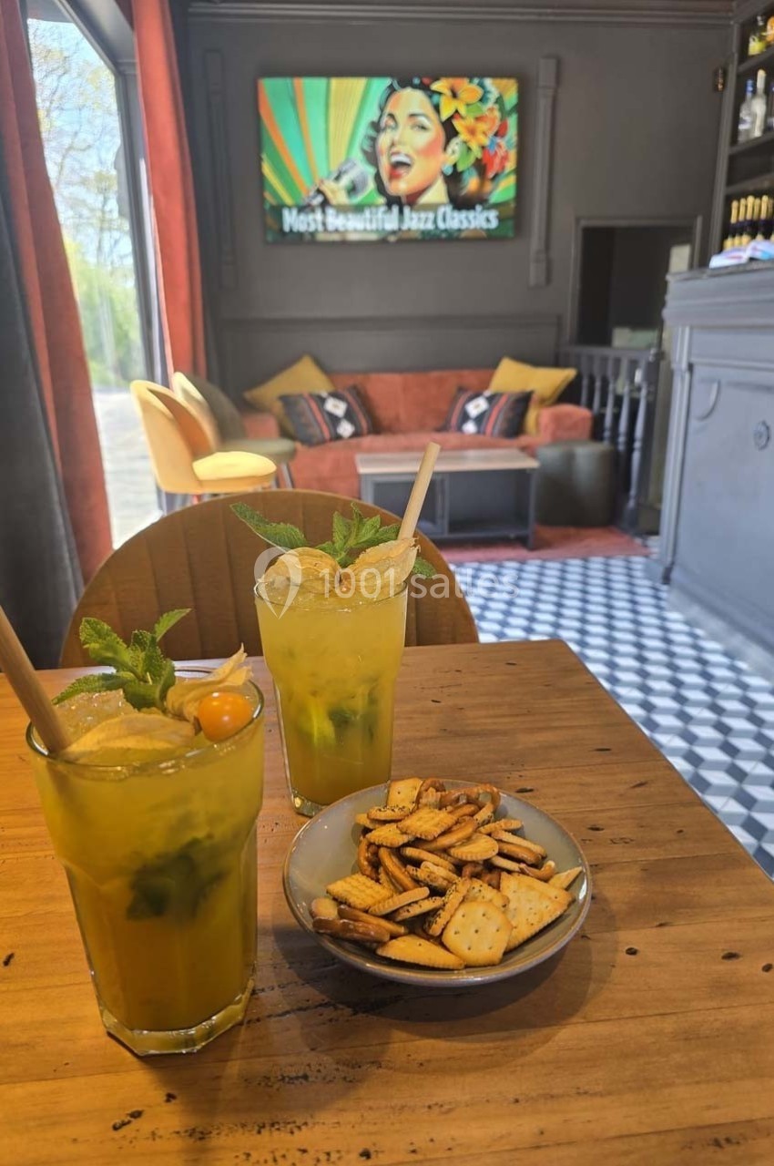 Deux cocktails jaunes garnis de menthe et physalis sur une table en bois avec un bol de biscuits, intérieur de café en…