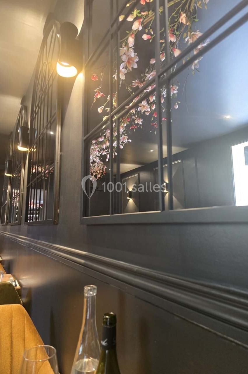 Miroirs encadrés reflétant des fleurs suspendues dans un intérieur sombre et élégant avec des lumières murales.