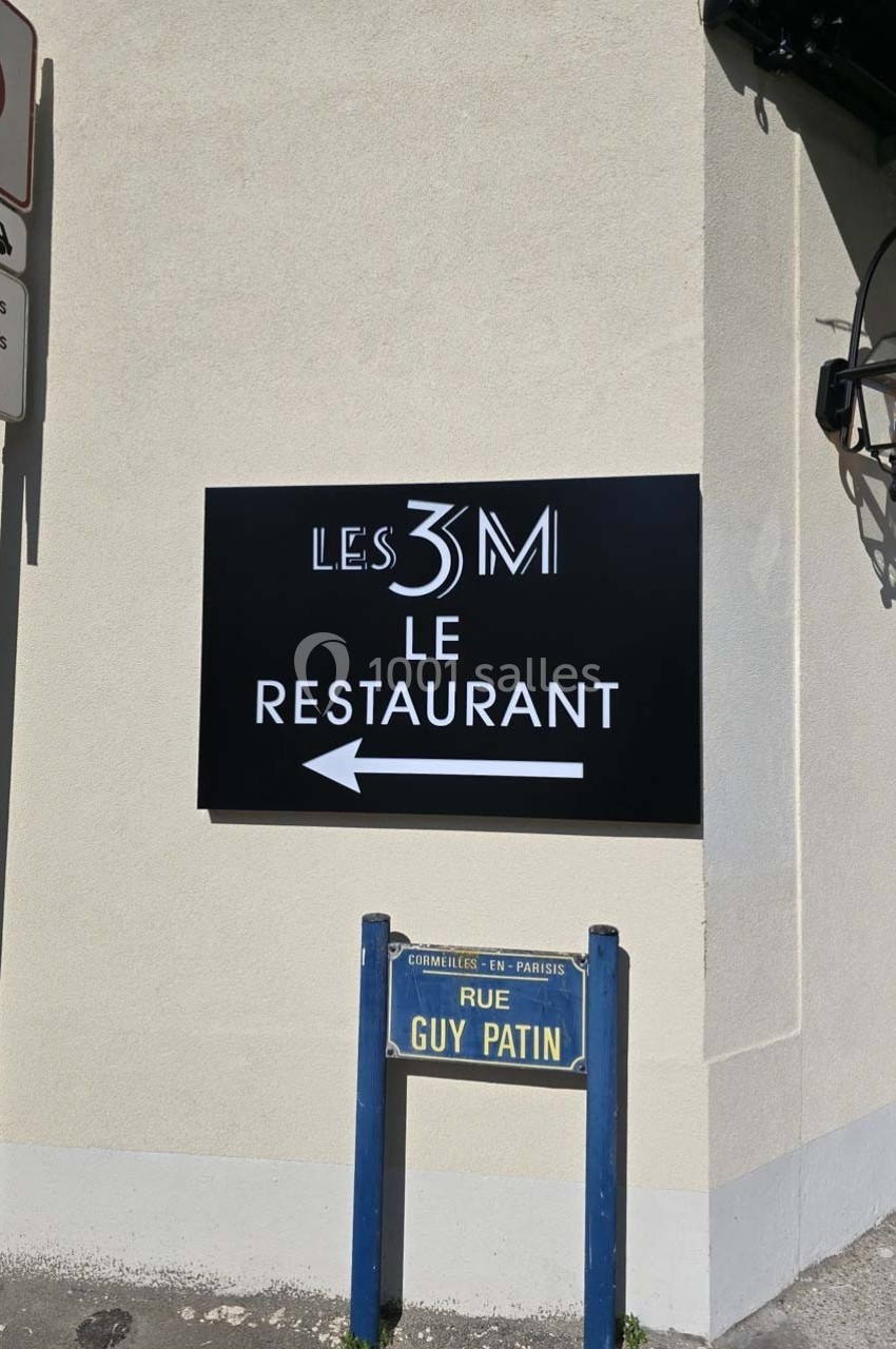 Panneau indiquant ’Les 3M Le Restaurant’ avec une flèche, situé à l'angle d'une rue nommée Guy Patin.
