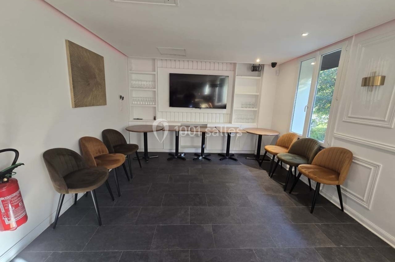 Salle lumineuse avec chaises disposées en cercle, tables pliées contre le mur, écran mural et extincteur visible.