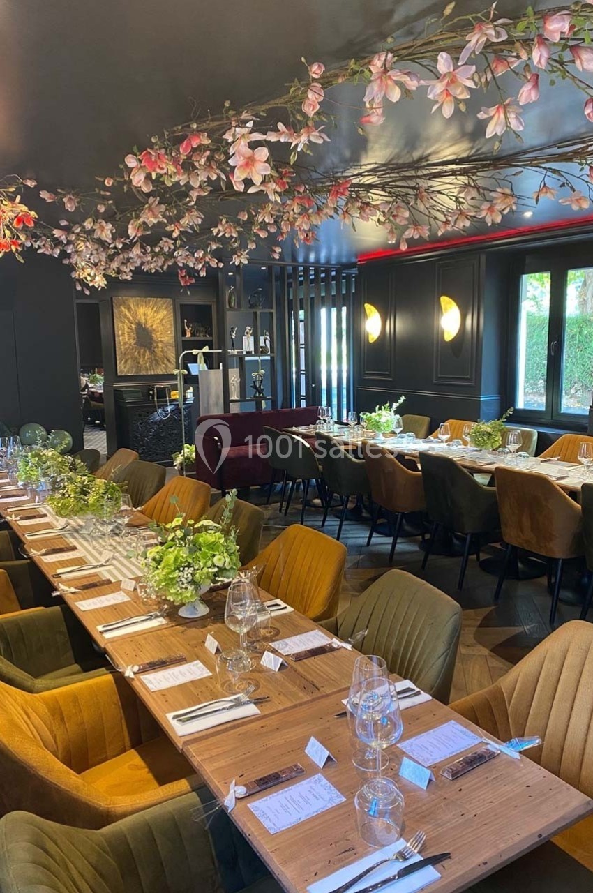 Salle de restaurant élégante avec longues tables en bois, chaises colorées et décoration florale suspendue.