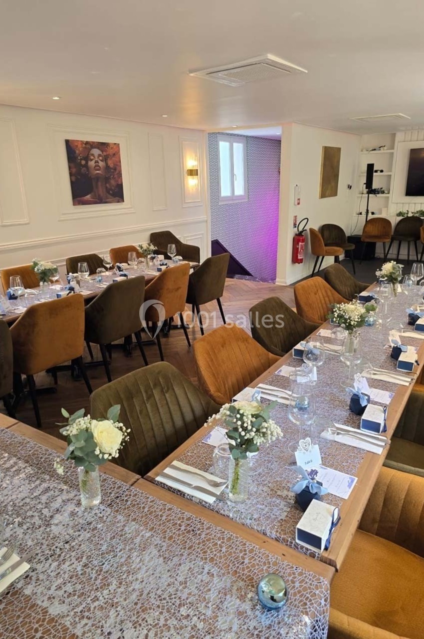 Salle élégamment décorée avec des tables dressées, des chaises rembourrées et des fleurs en centre de table.