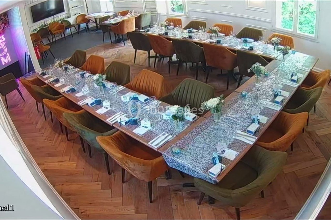 Salle de réception avec tables en U dressées, nappes bleues, chaises colorées et décoration florale.