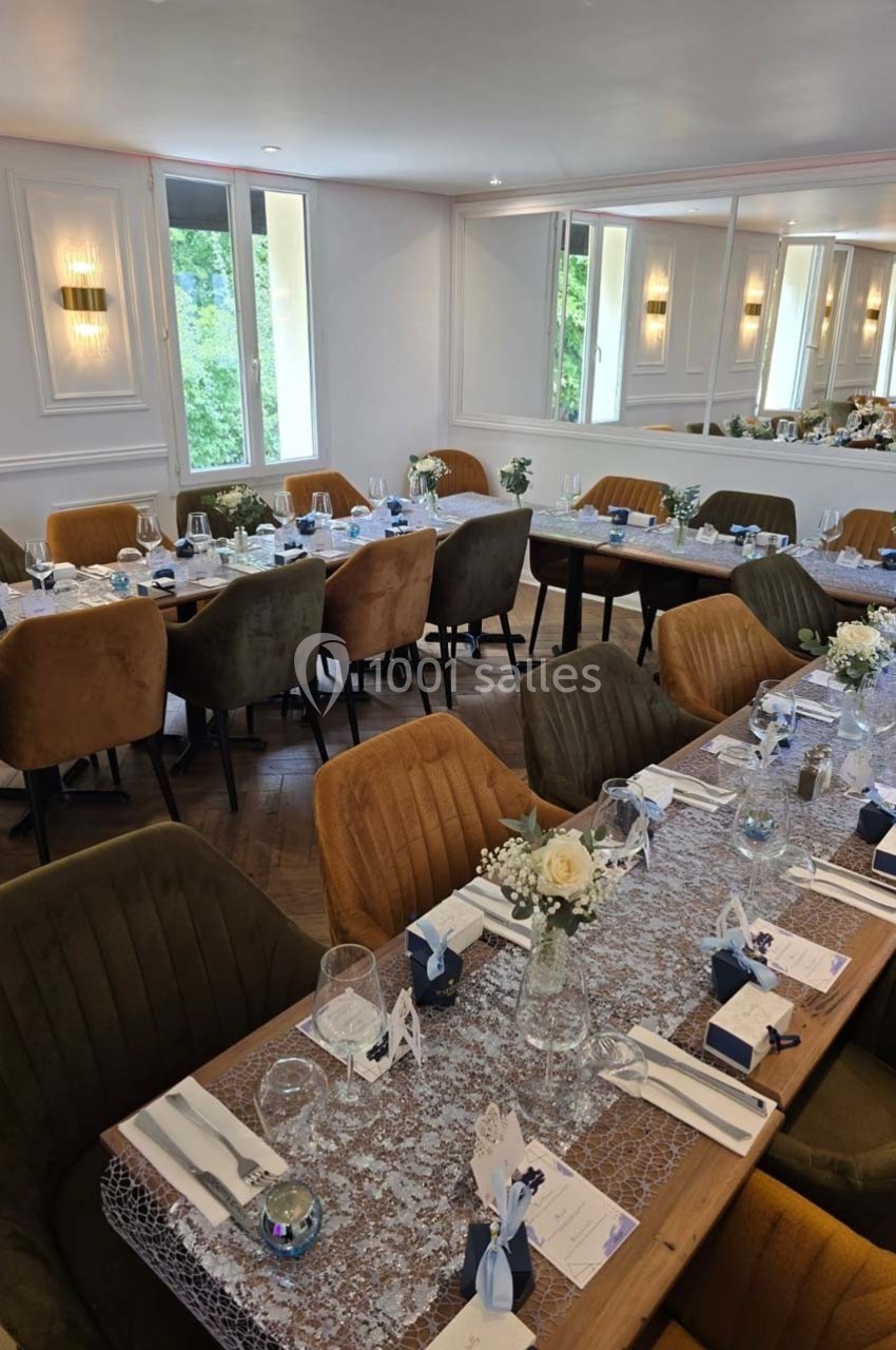 Salle de réception lumineuse avec tables décorées de nappes en dentelle, fleurs et couverts pour un événement.