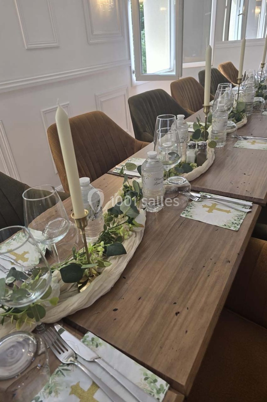 Table décorée pour un repas, avec bougies, verres, bouteilles d'eau et ornements végétaux sur un chemin de table.